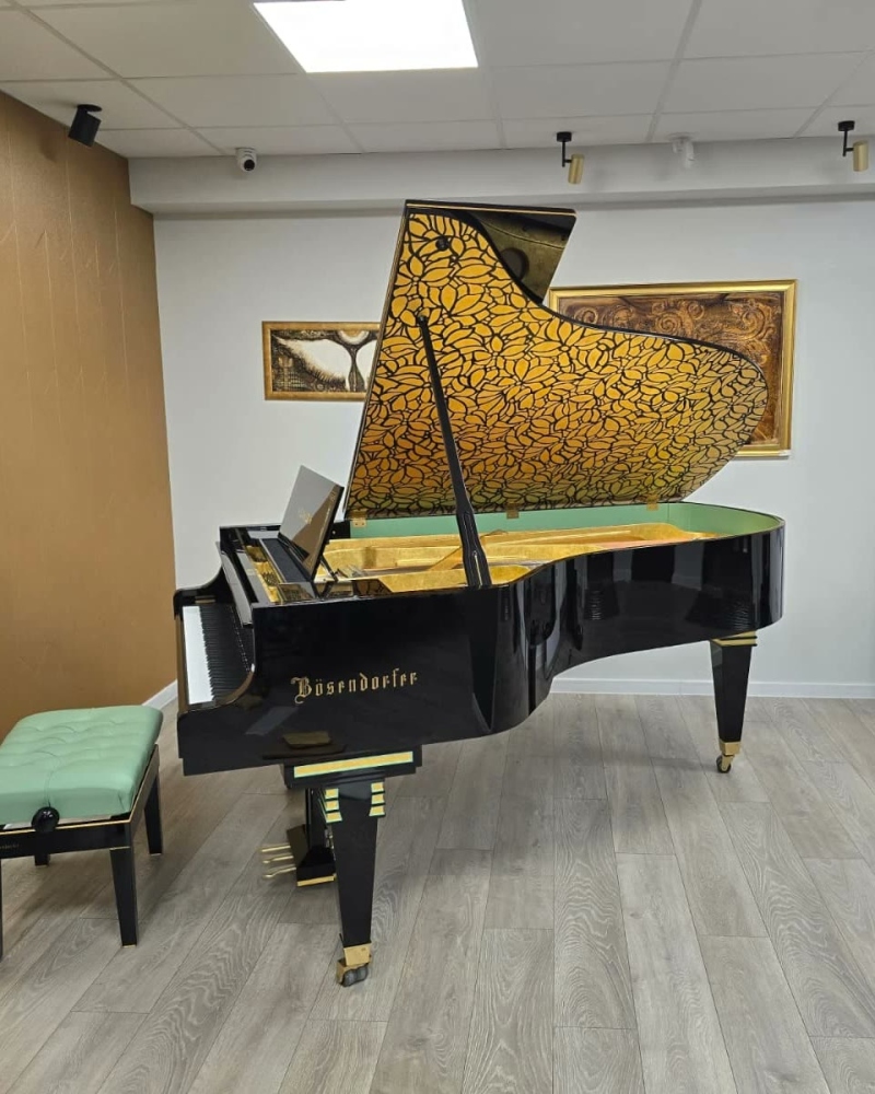 Pian cu coadă Bösendorfer negru, cu interiorul capacului decorat cu frunze aurii, montat într-o sală