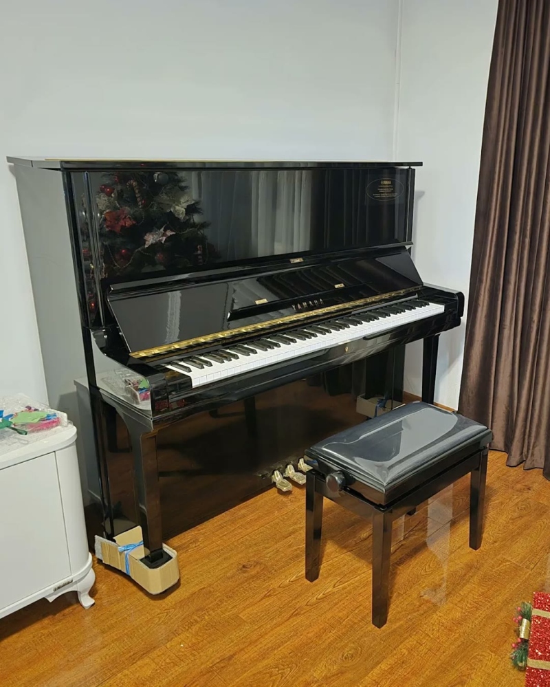 Pianină Yamaha neagră și o bancă de pian, lângă draperii, într-o cameră de zi